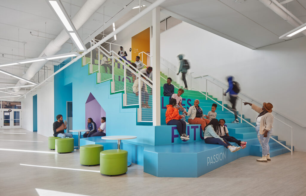 Blue and green colorful stairway inside BUILD Chicago with adjacent seating area shows teens sitting on steps.